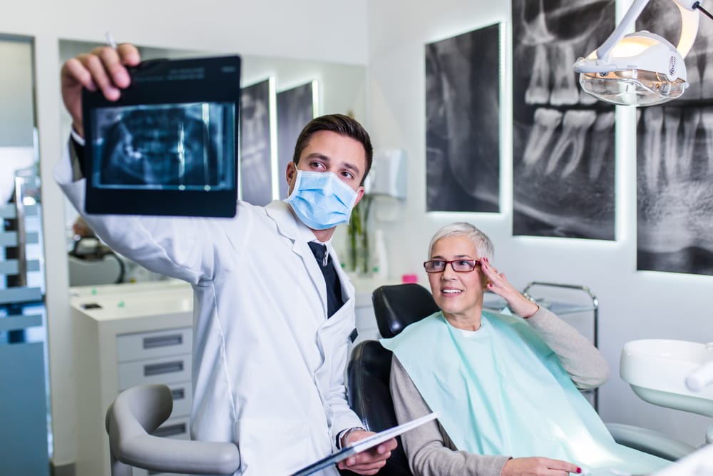 Dentist Reviewing X-Ray with Patient Post-Procedure – What to Expect After Dental Implant Surgery Male dentist in a mask showing a dental X-ray to an older female patient in a clinic chair during a consultation – What to Expect After Dental Implant Surgery
