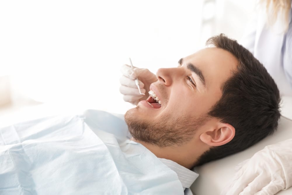 Young Male Patient Smiling During Whitening Procedure – Zoom! Teeth Whitening Smiling male patient reclining in a dental chair as a dentist prepares for a whitening treatment – Zoom! Teeth Whitening