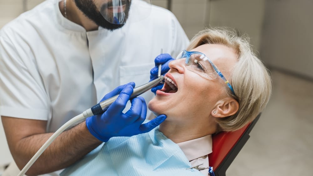 Patient Undergoing In-Office Whitening Treatment – Zoom! Teeth Whitening Female patient wearing protective glasses receiving professional dental whitening treatment in a clinic chair – Zoom! Teeth Whitening