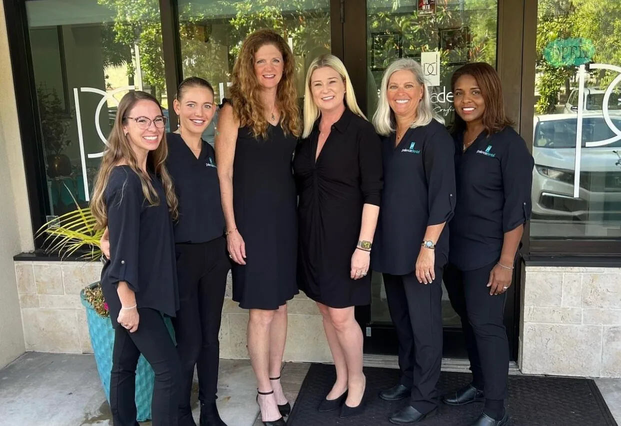 Dr. Stephanie Kinsey and Her Staff Smiling in Front of Office – Palencia Dental Dr. Stephanie Kinsey, standing with her five smiling staff members in black outfits, outside the Palencia Dental office – Palencia Dental