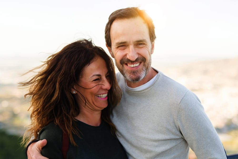 Smiling middle-aged couple outdoors enjoying the sunshine and each other’s company, radiating confidence and well-being – What to Expect After Dental Implant Surgery 