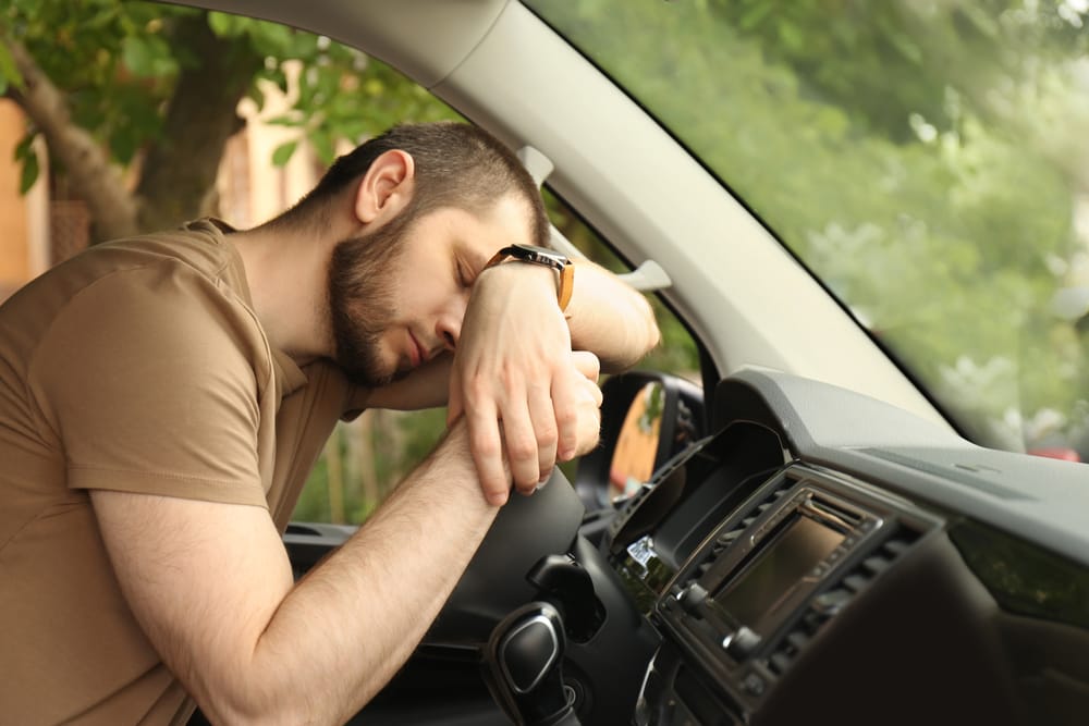 Driver Asleep Behind the Wheel from Fatigue – Snoring Tired man resting his head on the steering wheel while parked, representing daytime sleepiness linked to snoring and sleep disorders – Snoring