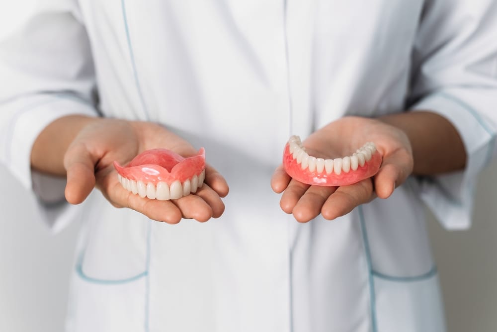 Close-up of a dental professional in a white coat holding a set of upper and lower full dentures in both hands – Dentures