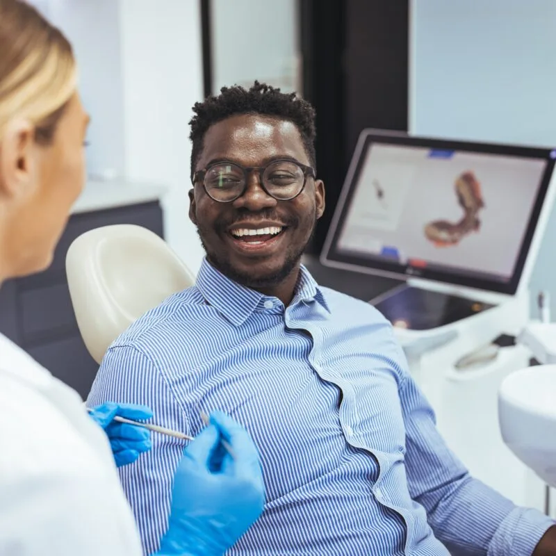 Smiling dental patient engaging with a gloved dentist in a modern clinic, with 3D dental imaging on screen, illustrating Palencia Dental’s personalized and innovative care approach