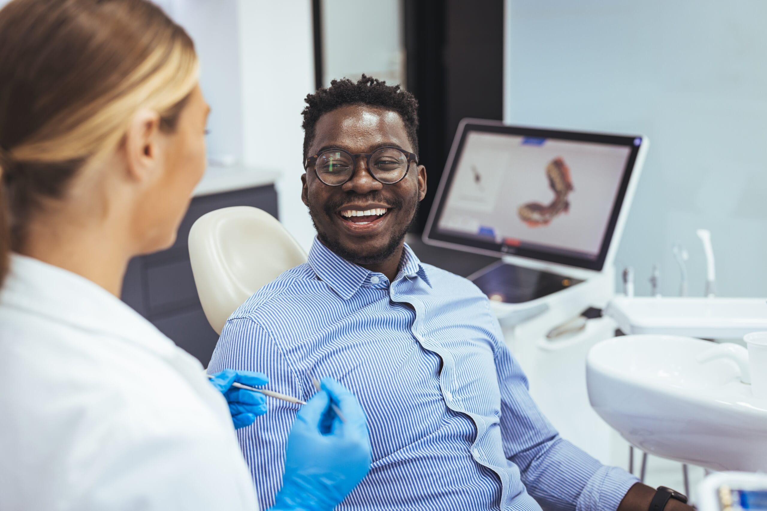 Smiling dental patient engaging with a gloved dentist in a modern clinic, with 3D dental imaging on screen, illustrating Palencia Dental’s personalized and innovative care approach